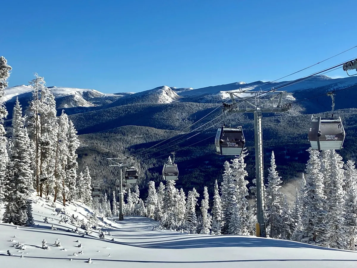 A scenic exterior view featuring ski lift gondolas gliding above snow-covered trees and a majestic mountain range, evoking the excitement of hitting the slopes and enjoying panoramic vistas.