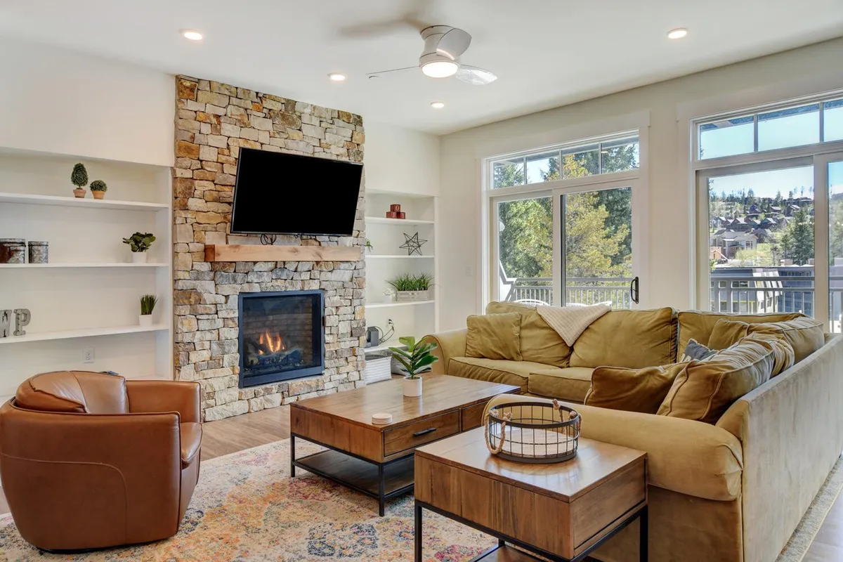 A stylish indoor seating area with a cozy fireplace, comfortable seating, a coffee table, and large windows letting in ample light. The overall mood is welcoming and ideal for gathering or relaxing.