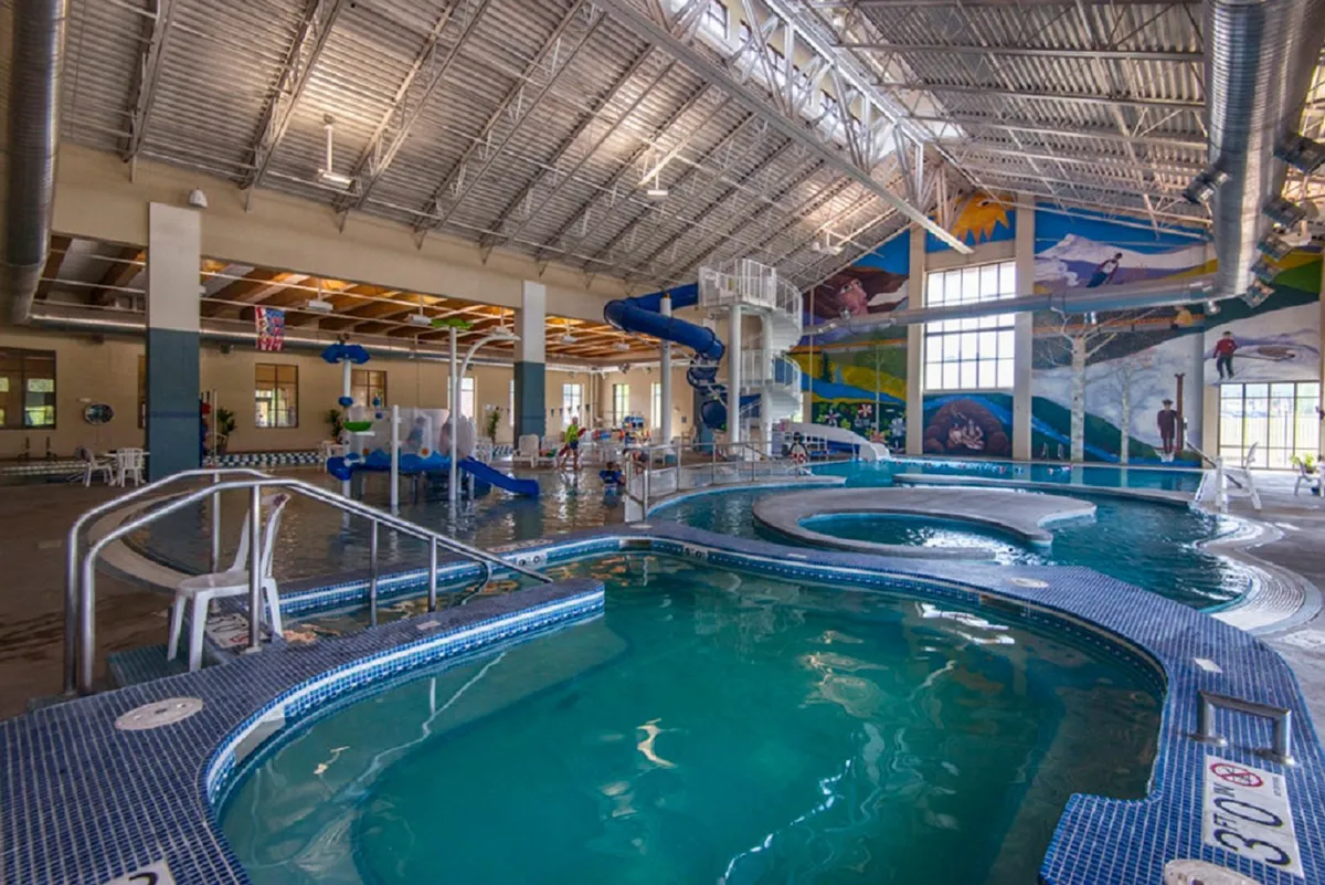 A vibrant indoor aquatic space featuring water slides, pools, a colorful mural, and ample seating. The setting is energetic and family-friendly, ideal for fun and recreation.