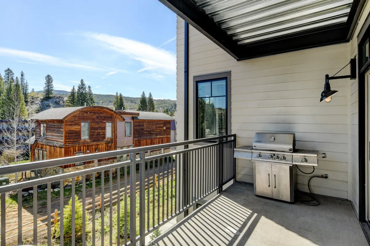 This image shows a private balcony area featuring a gas grill, surrounded by trees and with a neighboring cabin visible nearby. The setup is casual and inviting, with the grill positioned for easy outdoor cooking and a sense of privacy afforded by the natural backdrop.